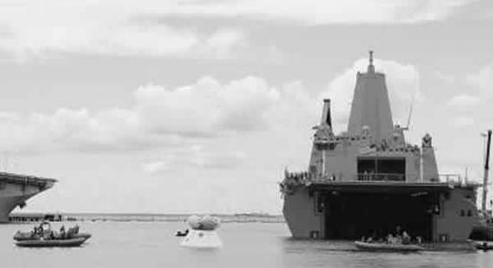 漂浮在海上的白色舱体为“猎户座”飞船模拟载人舱，海军正牵引着载人舱向“阿灵顿”号两栖船坞运输舰方向移动。