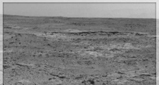 在这个场景的中间位置，位于地平线前方的一道低矮的隆起看起来像是一条黑带子，这道隆起就是火星上的露出岩“库珀斯敦”，这里可能是美国宇航局的“好奇”号利用机械臂上的