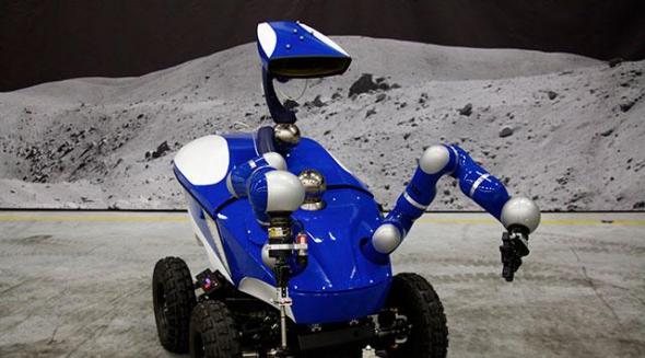 欧空局空间研究与技术中心(ESTEC)内的机器人漫游车“蓝虫”，背景图是灰色的月球山丘，它在国际空间站宇航员的操作下完成了此次试验。