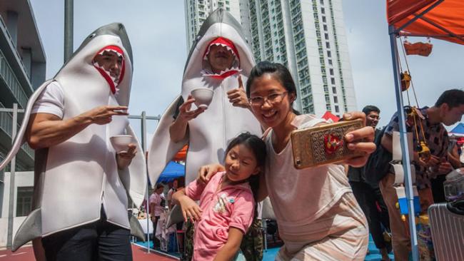 一对母女在素食嘉年华会上摆姿势拍照，两个男生打扮成鲨鱼推广素食鱼翅汤。中国年轻一代对动物福祉的观念和保育意识愈来愈高。 PHOTOGRAPH BY ALEX H