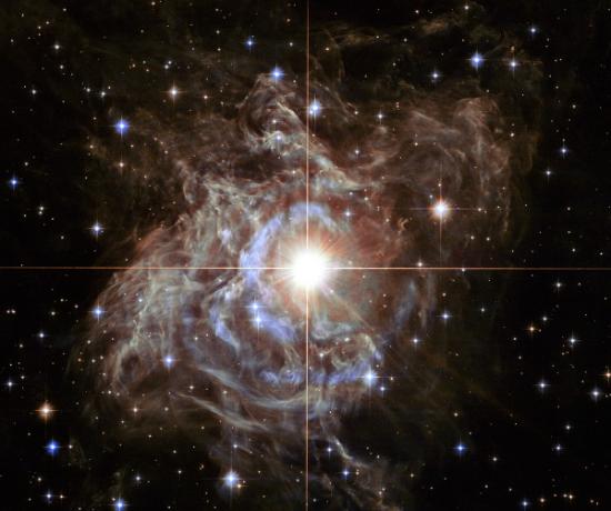 这张NASA发表的哈勃太空望远镜观测影像，仿佛是闪耀星芒所交织的耶诞花圈。图中这颗明亮的变星「船尾座RS星」，周围包覆着一层会反射恒星光芒的茧状尘埃，这些气体微