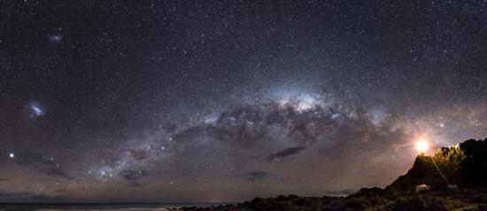 银河系的中心地带，距离地球约2.6万光年，充满了尘埃和无数的小恒星。新西兰帕利斯尔角的一座灯塔照亮了昏暗的银河系，点点星光闪耀在海面上，浪漫异常。
