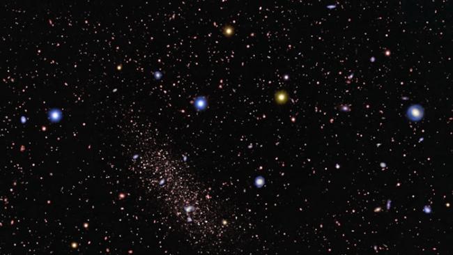 一个距离地球1100万光年的矮球状星系（左中）在邻居大星系引力拖拽下被拉长。