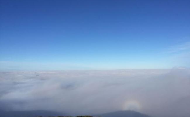 蓝天下山间被浓雾覆盖，彩虹光环罩住的人影屹立在山脊。