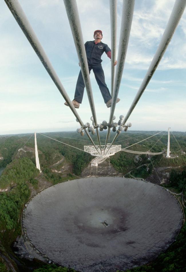 1989年，技术员路易斯．埃雷迪亚（Luis Heredia）正在阿雷西博天文台检查将接收器悬挂在射电望远镜天线上的钢缆。 PHOTOGRAPH BY ROGE